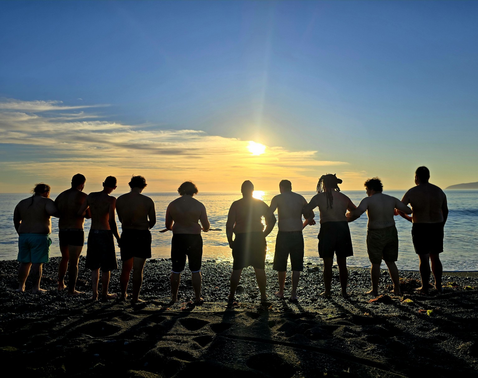 Whānau standing together beside the moana at sunrise